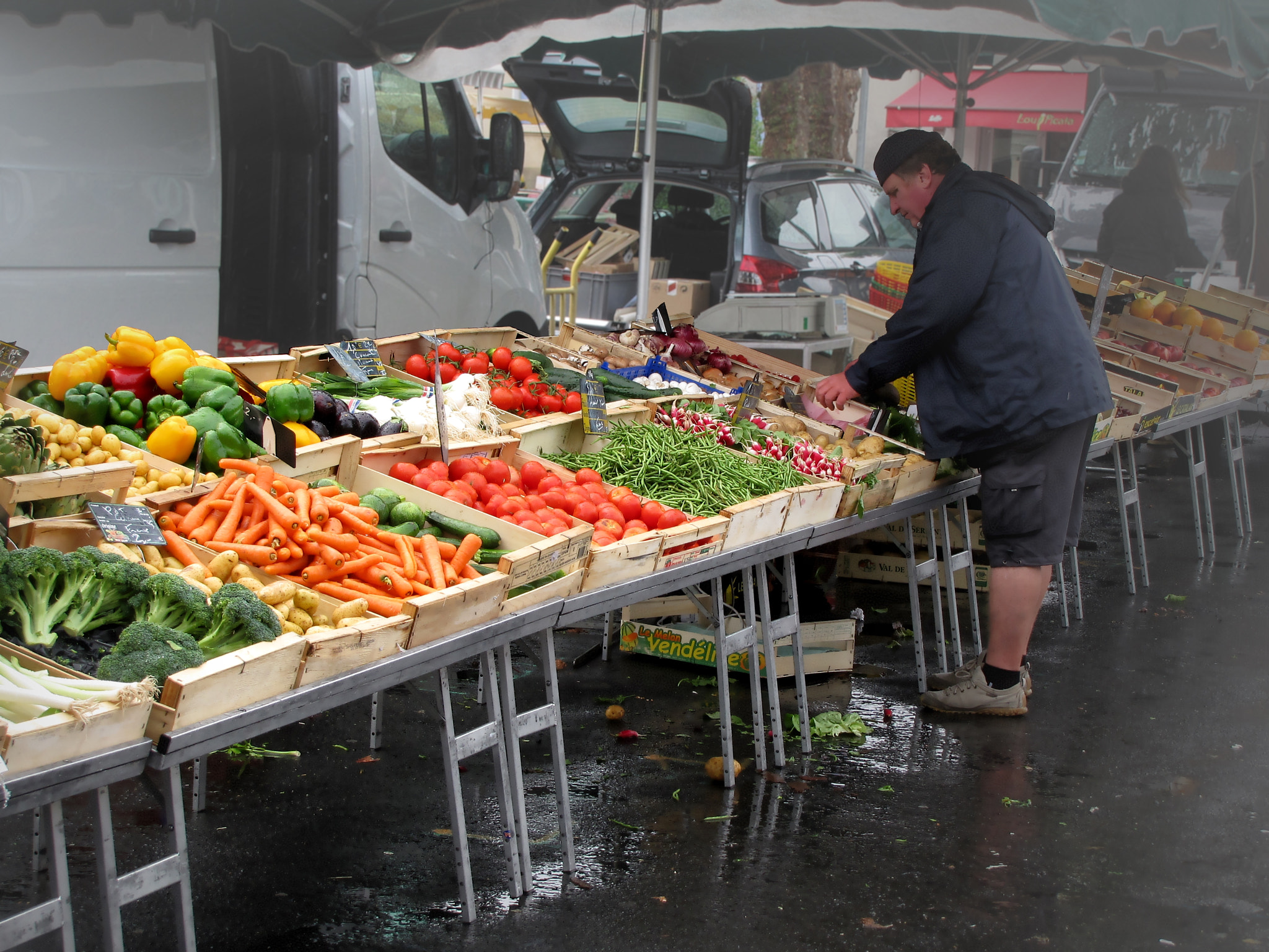 commerçante à l'étal d'un marché en France, fruits et légumes exposés devant elle