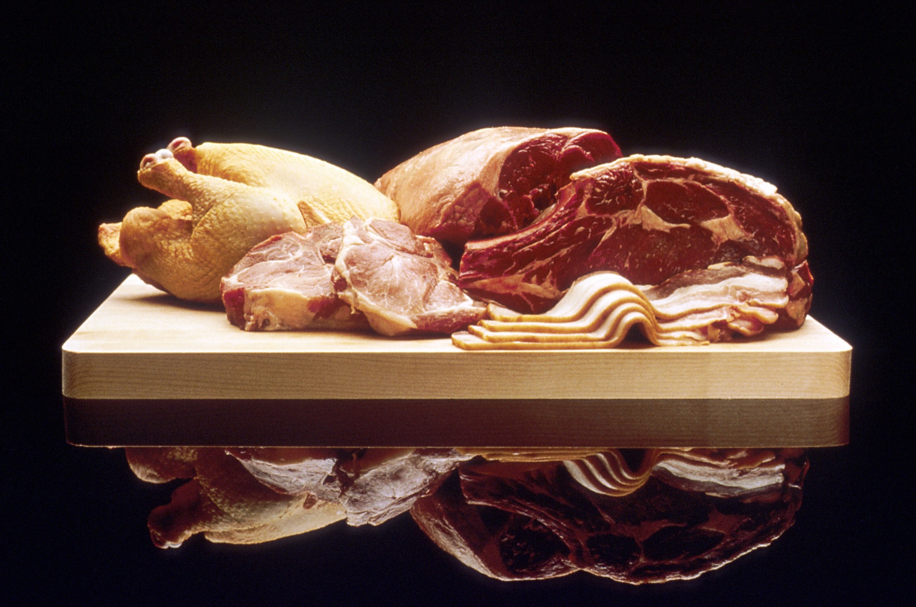 volaille, bœuf et porc crus disposés sur une planche à découper, base d'une ration crue pour chien