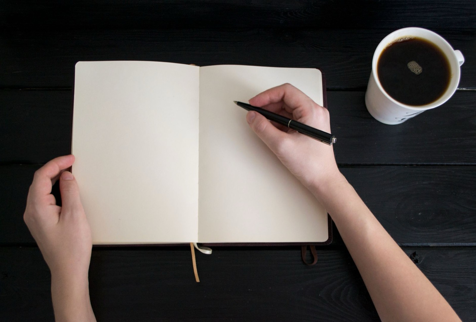 Des mains posées sur un carnet ouvert à côté d'une tasse de café